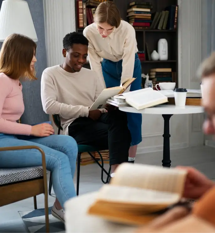 A group of young adults sitting together in a comfortable setting, reading books and discussing ideas