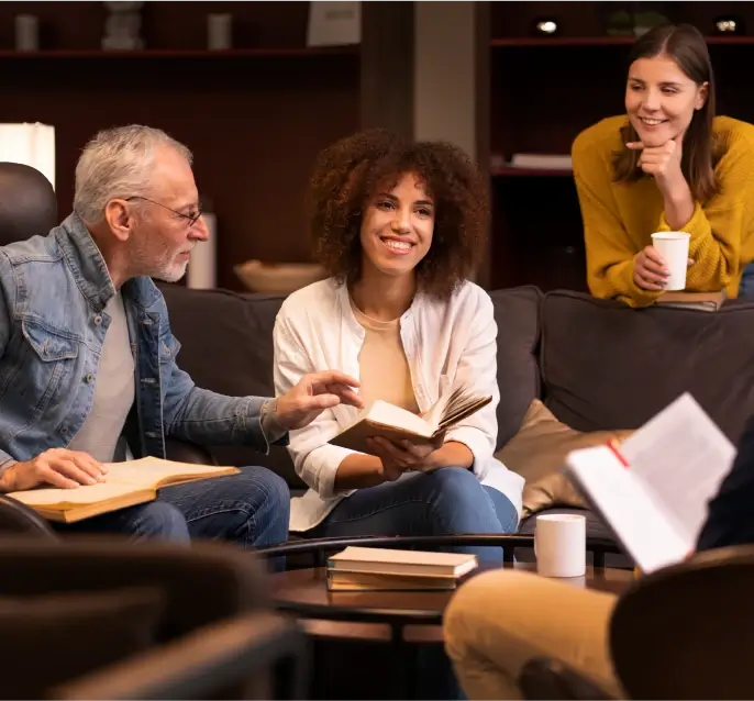 A diverse group of people sitting on and around a sofa, reading books and discussing ideas